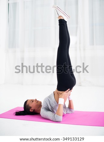 Fit woman doing shoulder stand on mat practising yoga health and fitness concept.