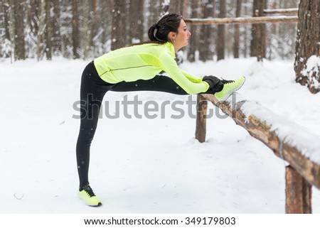 Winter training Fitness model athlete girl warm up stretching her hamstrings, leg and back
