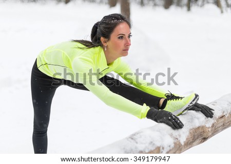 Fitness model athlete warm up stretching her hamstrings, leg and back. Young woman exercising outdoors winter in park