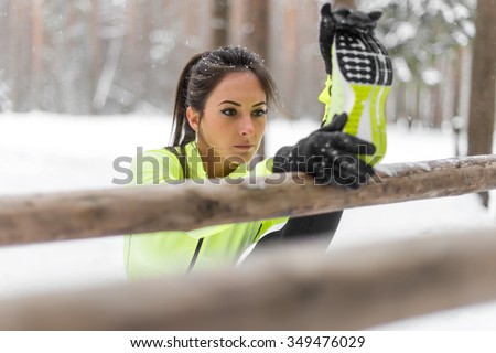 Fit woman athlete doing hamstring leg stretching exercises outdoors in woods. Female sports model exercising outdoor winter park