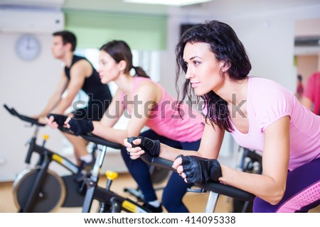 Group training people biking in the gym, exercising legs doing cardio workout cycling bikes.