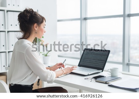 Rear view portrait of a businesswoman sitting on her workplace in the office, typing, looking at pc screen.