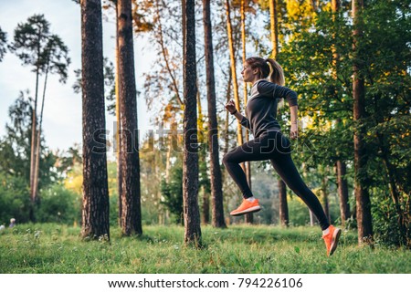 Young female athlete jogging in forest. Jogger doing morning physical training.