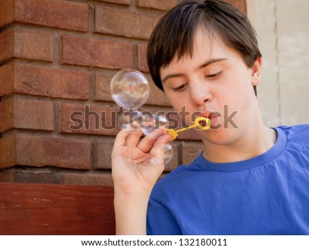 horizontal orientation close up of boy with autism and down's syndrome outside playing with bubbles and copy space / Boy with Bubbles