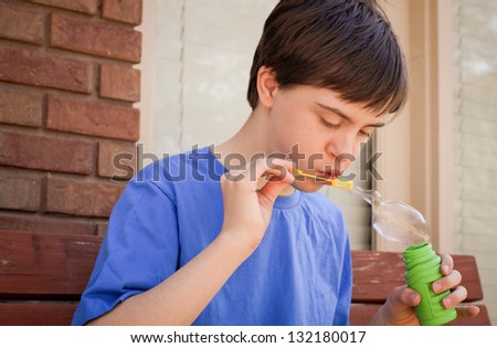 horizontal orientation close up of boy with autism and down\'s syndrome outside playing with bubbles and copy space / Bubbles as Sensory Play