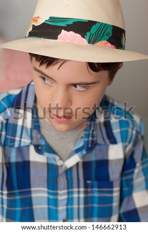 vertical orientation close up of a boy with autism and down\'s syndrome in a blue plaid shirt and straw hat with floral band looking away from the camera / Fashionable Boy Tourist