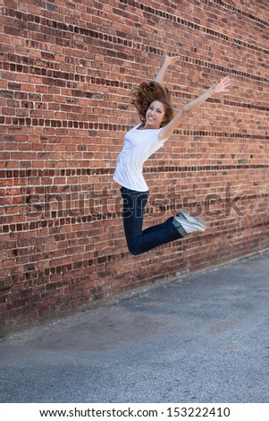 vertical orientation of happy, beautiful,  teenage girl jumping for joy with vintage brick patterned background and copy space / Teenage Girl Jumping for Joy