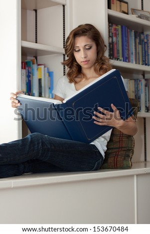 vertical orientation close up of a beautiful young woman in a library setting holding a large open book with copy space / Successful Learning Environment
