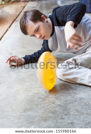 vertical orientation of a boy with autism and down\'s syndrome looking intently at a round, yellow, object he is spinning on a cement floor, with copy space /  Signs of Autism