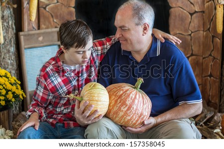 horizontal orientation close up of a boy with autism and down\'s syndrome and his smiling Dad, seated together holding pumpkins with copy space / Father and Son Choose Pumpkins