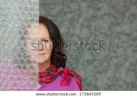 horizontal orientation of a woman in brightly colored business attire with a slight smile and one half of her face blurred by a textured surface / Hidden from View