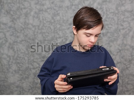 horizontal orientation of a boy with autism and down's syndrome sitting down, holding a tablet device in both hands as he looks at the screen / Apps for Visual Learners