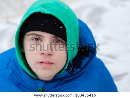 horizontal orientation close up of a boy with autism and down's syndrome dressed in a colorful hat, sweatshirt and jacket, with snowy background / Helping the child with Autism Dress Appropriately