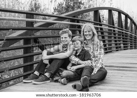 horizontal orientation of a beautiful woman sitting with her two sons outside on a bridge in black and white with copy space / Making Time for Each Other