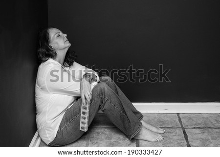 horizontal orientation close up, in black and white, of a single woman sitting in a corner with a pill box in one hand, looking exhausted / Finding the Right Medication