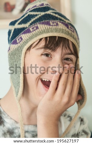 vertical orientation close up of a teenage boy with autism and down\'s syndrome, wearing a winter wool hat, with his hand on his face, looking surprised and happy / Surprised Teenage Boy