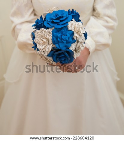 vertical orientation close up of a bride in a vintage wedding gown, holding a bouquet of hand made,  paper flowers in royal blue and off white printed paper, with copy space / Vintage Wedding Gown