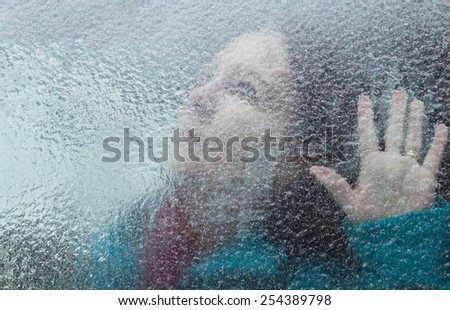 horizontal orientation of an attractive woman looking out through a window covered with thick ice, with her hand at the window / Memory Loss