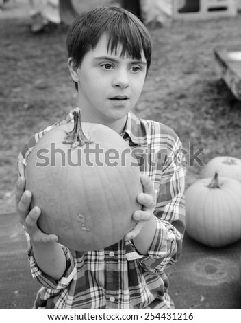 vertical orientation black and white image of an attractive teenage boy with autism and down\'s syndrome holding a pumpkin / Fall Activities for Children with Autism
