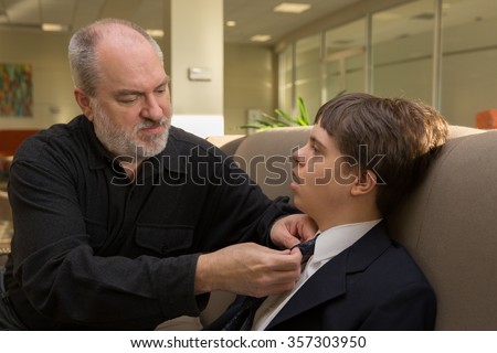 horizontal orientation close up of a father helping his son with disabilities put on a necktie / Father helping son with autism and Down\'s Syndrome with a necktie