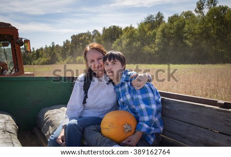horizontal orientation color image with shallow depth of field, with a happy mother and her son with autism and down\'s syndrome on a hay ride / Choosing a pumpkin with Mom