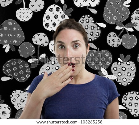Portrait of a young beautiful woman with a surprised face with her hand over her mouth over black and white fruits background.