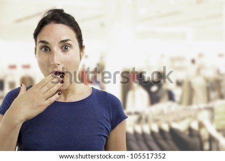 Young beautiful woman covering her mouth with her hand in a surprised pose over a shop background