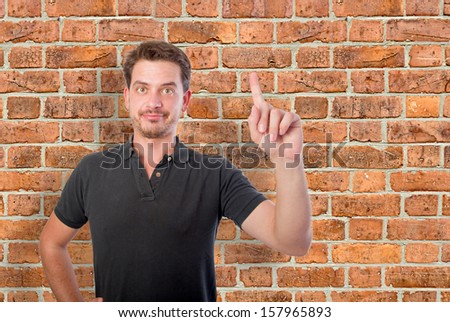 Young man pointing up with his finger over a bricks wall