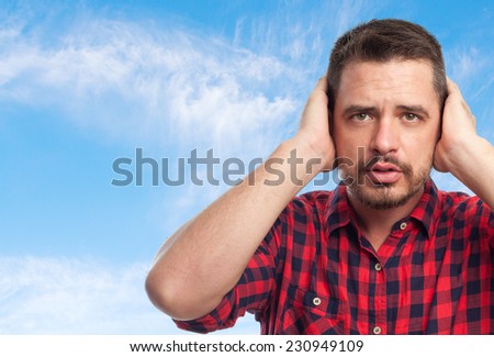 Young man with squares shirt over clouds background. Covering his ears