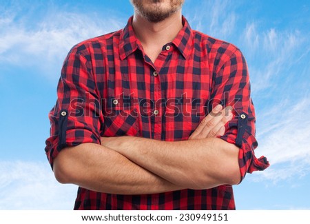 Young man with squares shirt over clouds background. With arms crossed