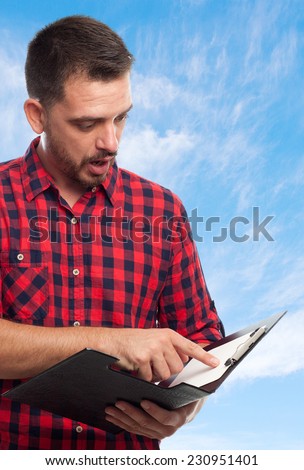 Young man with squares shirt over clouds background. Reading from a black folder