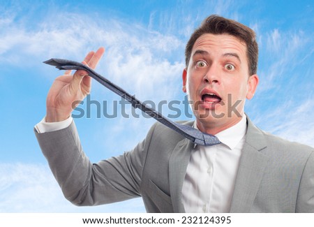Young business man with grey suit over clouds background. Pulling his tie
