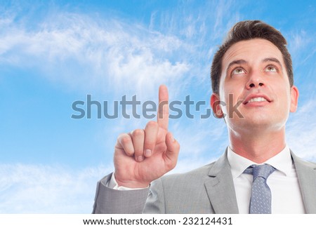 Young business man with grey suit over clouds background. Pointing up with his finger