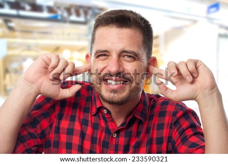 Man with red shirt over shopping center background. Looking upset because of the noise