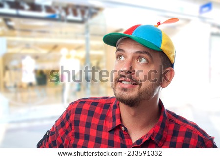 Man with red shirt over shopping center background. Wearing a colorful cap