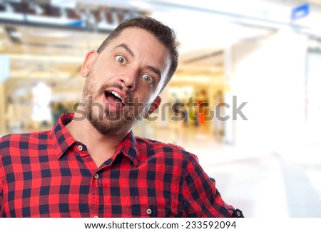 Man with red shirt over shopping center background. Looking surprised