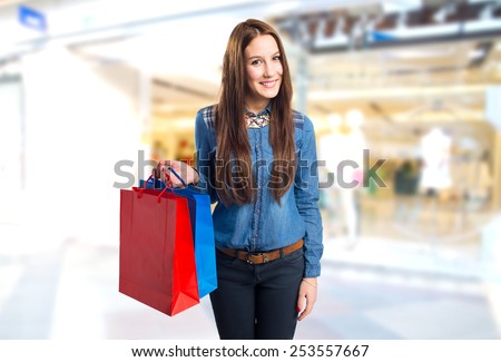Trendy young woman holding red and blue shopping bags. Over shopping center background