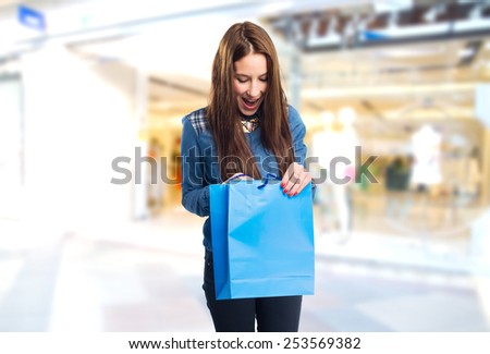 Trendy young woman looking surprised into a blue shopping bag. Over shopping centre background
