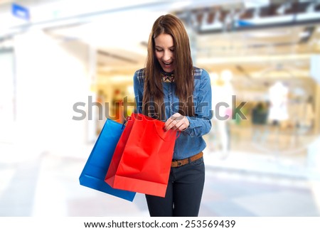 Trendy young woman with red and blue shopping bags. She looking surprised. Over shopping centre background