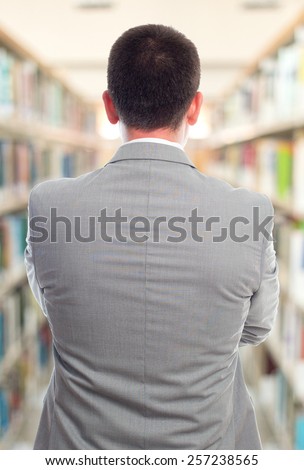 Business man with grey suit. He is giving his back. Over library background