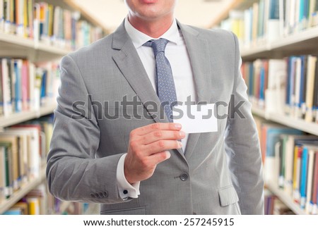 Business man with grey suit. He is holding a white card. Over library background