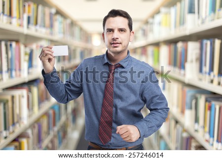 Man wearing a blue shirt and red tie. He is holding a white card.. Over library background