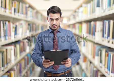 Man wearing a blue shirt and red tie. He is surprised looking into a black folder. Over library background