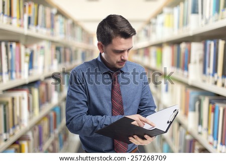 Man wearing a blue shirt and red tie. He is looking into a black folder. Over library background