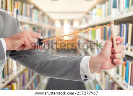 Man with grey suit closeup with slingshot. Over library background