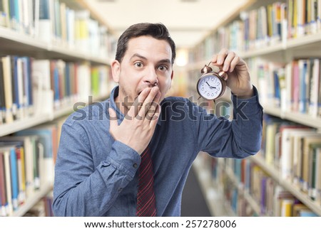 Man wearing a blue shirt and red tie. He is holding a clock. Over library background