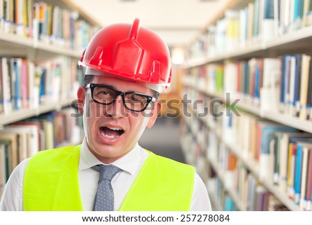 Architect man wearing a red helmet. He is looking funny. Over library background