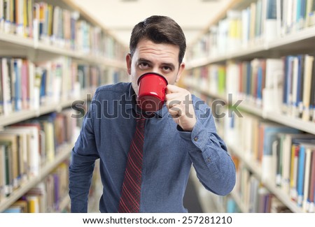 Man wearing a blue shirt and red tie. He is drinking from a red cup. Over library background