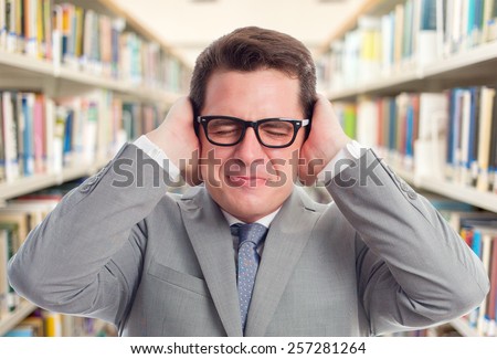 Business man with grey suit. He looks upset because of a noise. Over library background