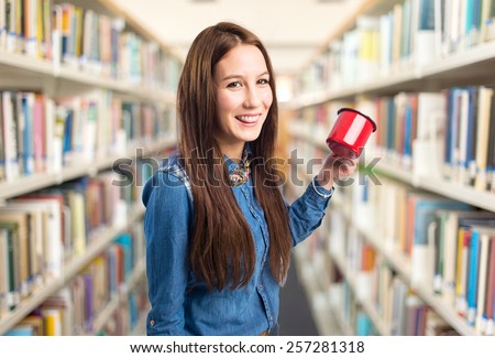 Trendy young woman holding a red cup and smiling. Over library background